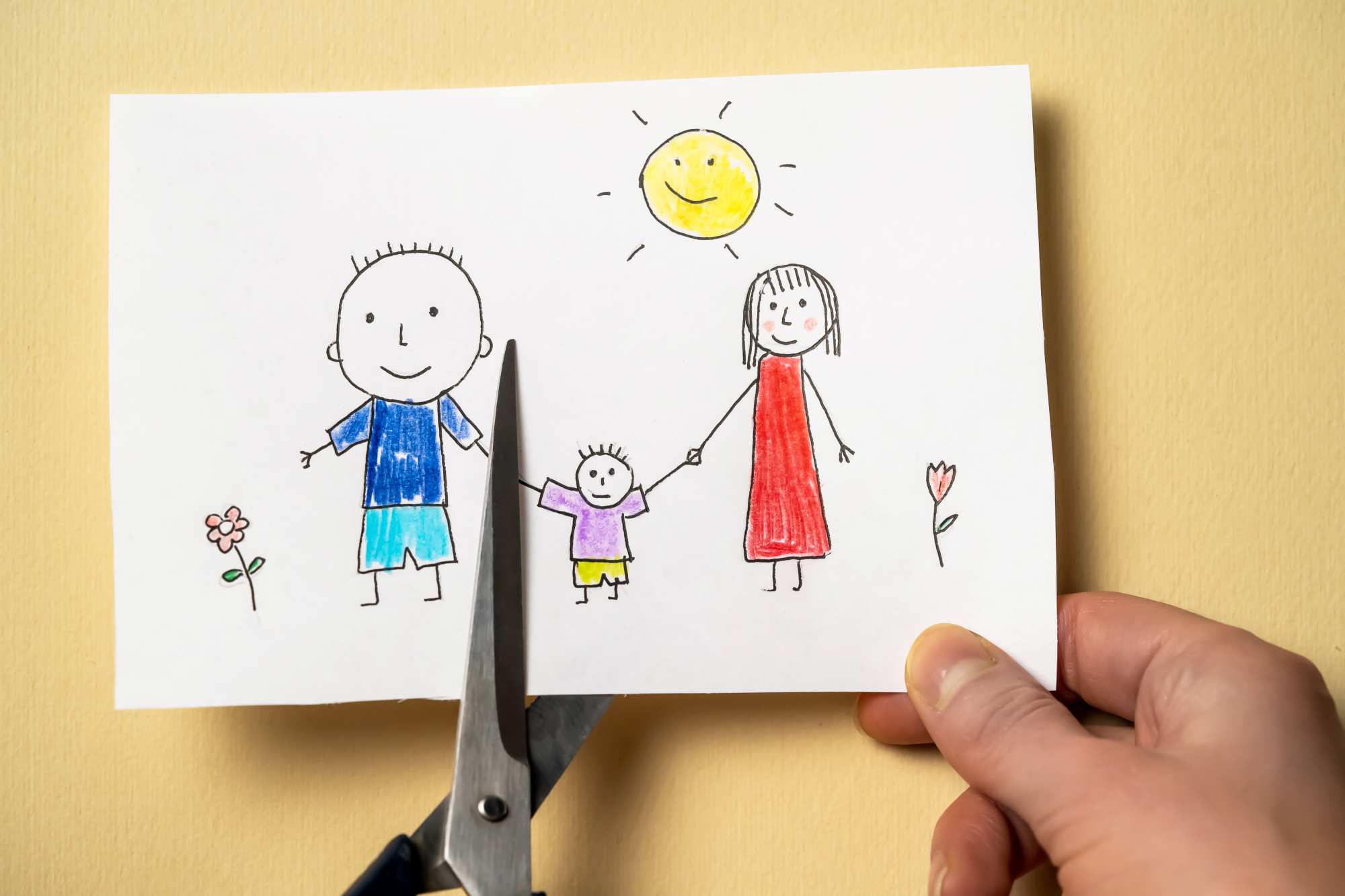 scissors cutting a paper of a child's drawing of their family to indicate divorce